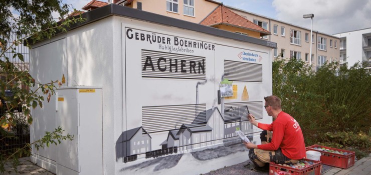 Das Motiv der dritten neu gestalteten Trafostation in der Böhringer Straße 1 erinnert an die Hohlglasfabriken Gebrüder Boehringer, die eine der ältesten Glashütten im süddeutschen Raum  waren.  Auf dem Foto ist der Künstler, Markus Ronge, bei seiner Arbeit zu sehen. 